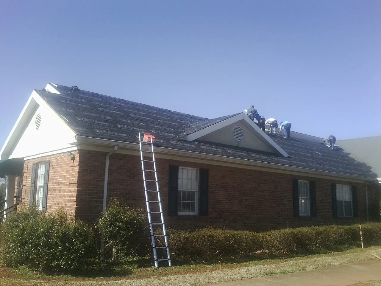 Crew tearing shingles off a brick ranch roof with a ladder set — Metal Roof Repair work by our crew in Union Mills