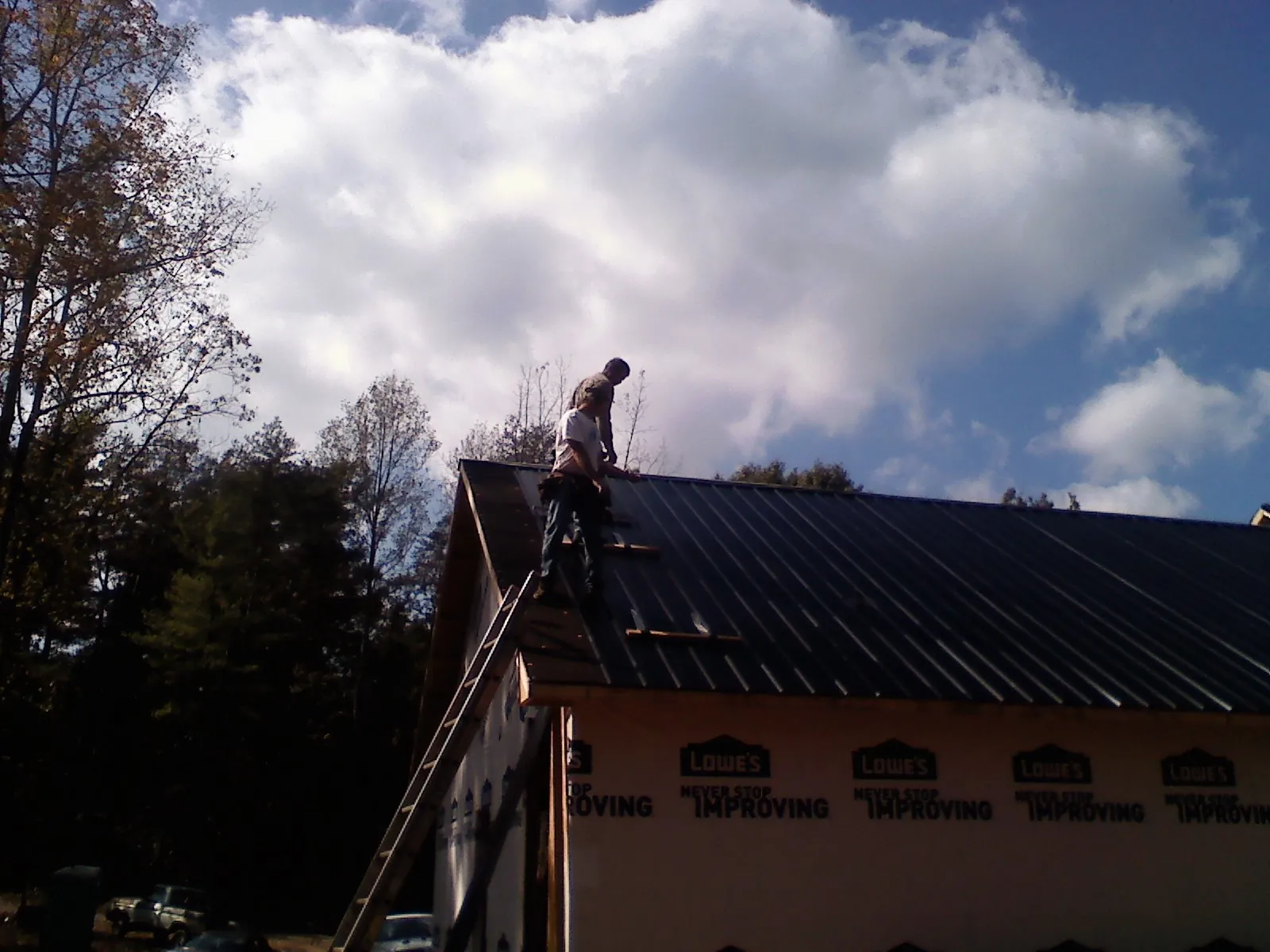 Roofer fastening dark metal panels high against a cloudy sky, from a Roof Inspection job in Union Mills