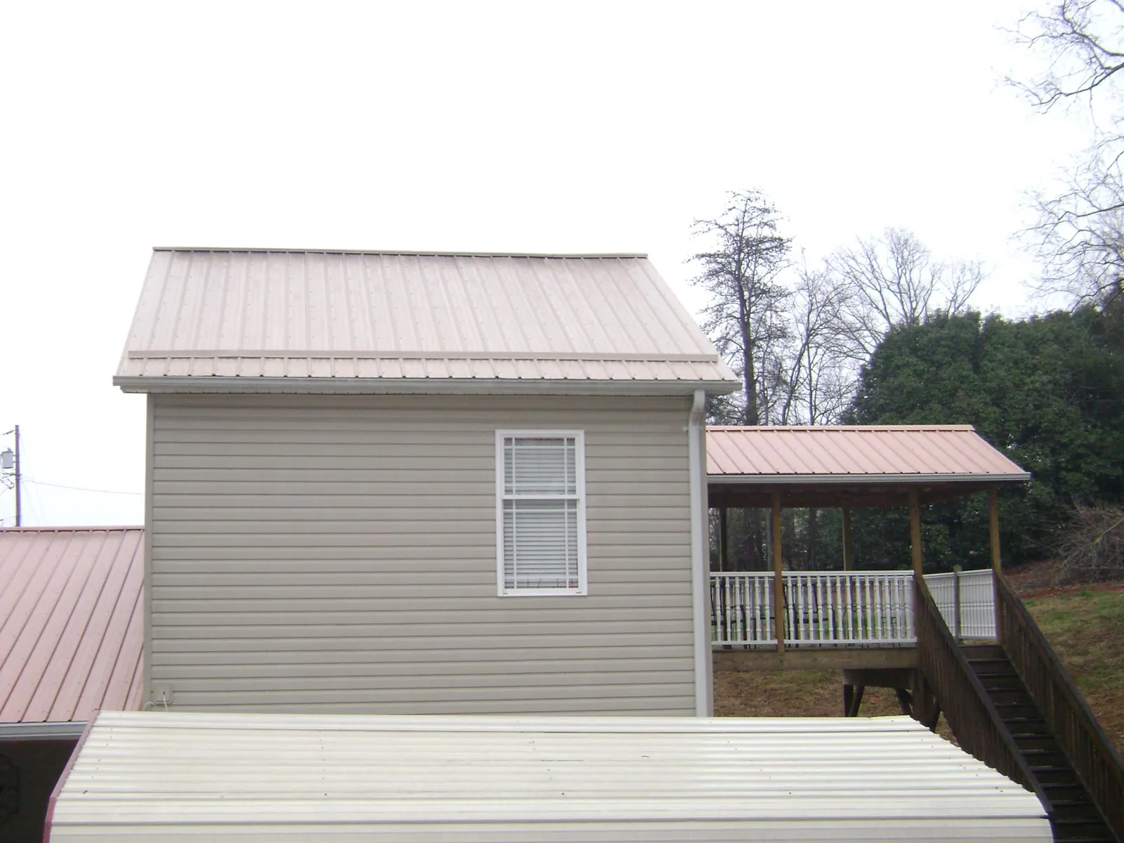 Tan metal roofs on a two story addition and attached porch, from a Roof Replacement job in Union Mills